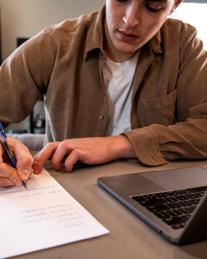 A person writing notes next to a laptop
